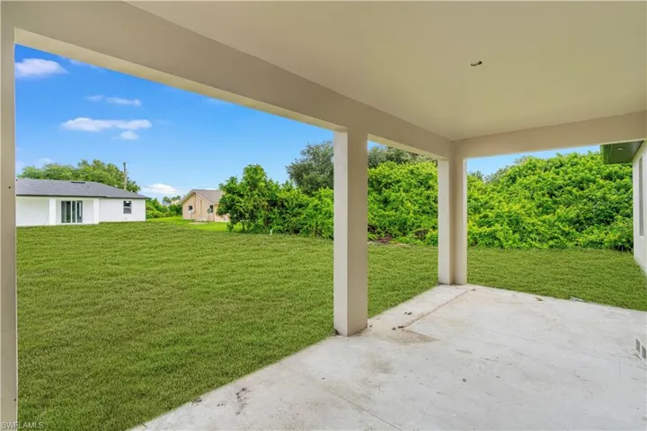 Covered patio with concrete flooring, support columns, and an expansive lawn