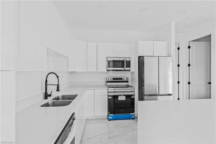 Kitchen featuring white cabinetry, quartz countertops, dual-basin sink with matte black gooseneck faucet, stainless steel appliances, and stone-finish flooring