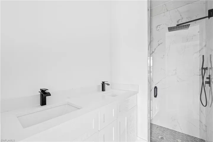Dual-sink vanity with white stone countertop, matte black fixtures, walk-in shower with floor-to-ceiling stone-tiled walls, glass enclosure, and rainfall showerhead