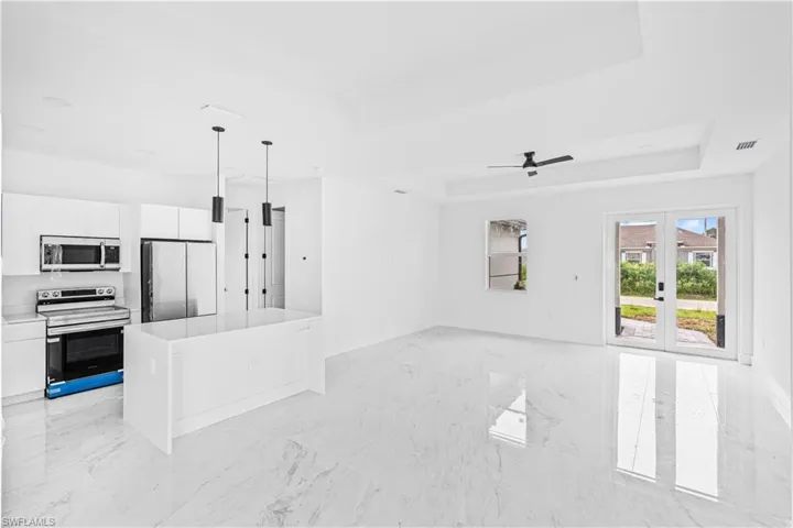 Open-concept kitchen and living area featuring high-gloss large-format flooring, white cabinetry, a center island with stone-finish surfacing, tray ceilings with recessed lighting, and glass-paneled double doors