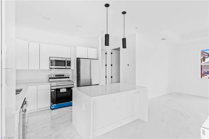 Kitchen featuring white cabinetry, an island with a stone-finish countertop, stainless steel appliances, and large-format tile flooring