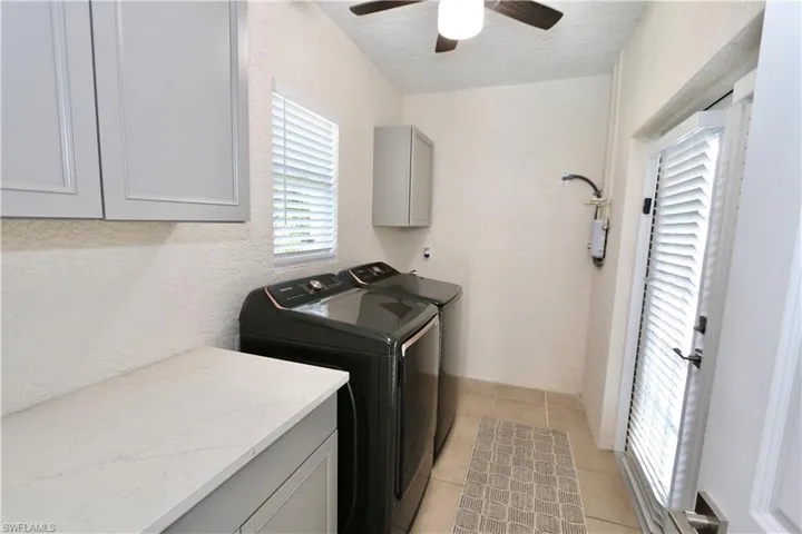 Laundry room featuring a textured wall, light tile patterned floors, washer and clothes dryer, a textured ceiling, and cabinet space