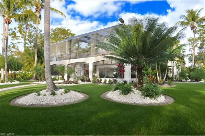 View of grassy yard featuring glass enclosure, a sunroom, and a balcony
