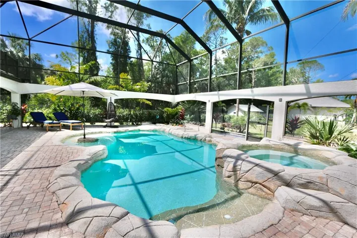 View of swimming pool with glass enclosure, a patio area, a sunroom, and a pool with connected hot tub