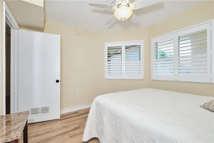 Bedroom featuring light wood-type flooring, a lighted ceiling fan, plantations shutters.