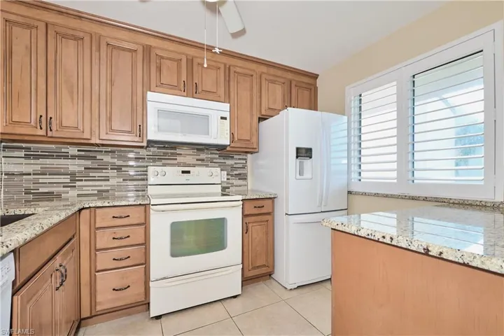 Kitchen with white appliances, light stone counters, brown cabinetry, and light tile patterned floors