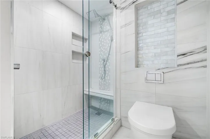 Bathroom featuring tile walls, toilet, and a shower with shower door