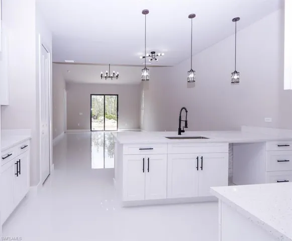 Kitchen featuring a peninsula, white cabinets, hanging light fixtures, and light stone countertops