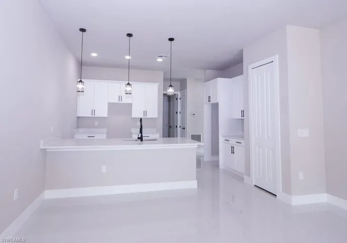 Kitchen featuring white cabinetry, a peninsula, pendant lighting, light stone counters, and a kitchen bar