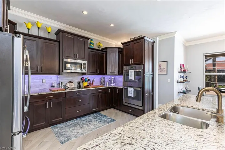 Kitchen with stainless steel appliances, a sink, backsplash, light stone countertops and crown molding