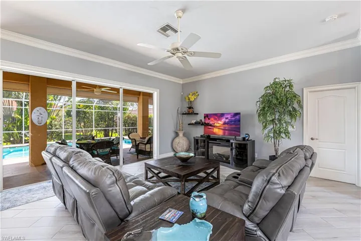 Living room featuring a ceiling fan, a sunroom, crown molding, and light tile flooring