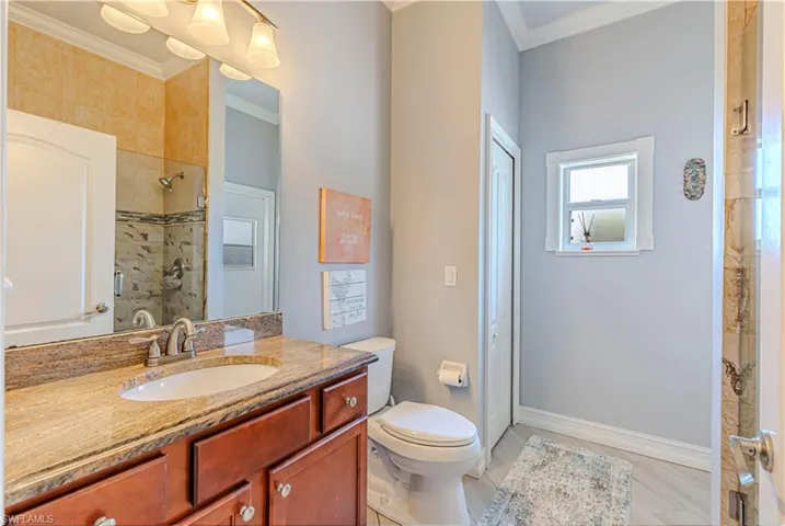 Full bathroom with ornamental molding, toilet, vanity, tiled shower, and baseboards