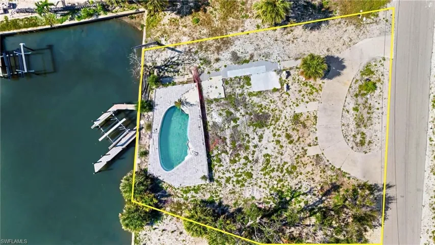 Aerial view of property and surrounding area with property boundaries highlighted, a pool, and a large body of water  - Virtually Edited Image