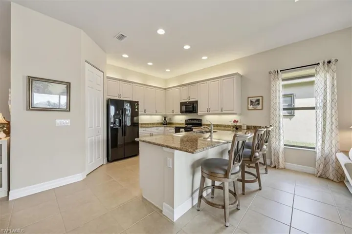 Kitchen featuring black appliances, light stone counters, a kitchen bar, light tile patterned floors, and recessed lighting