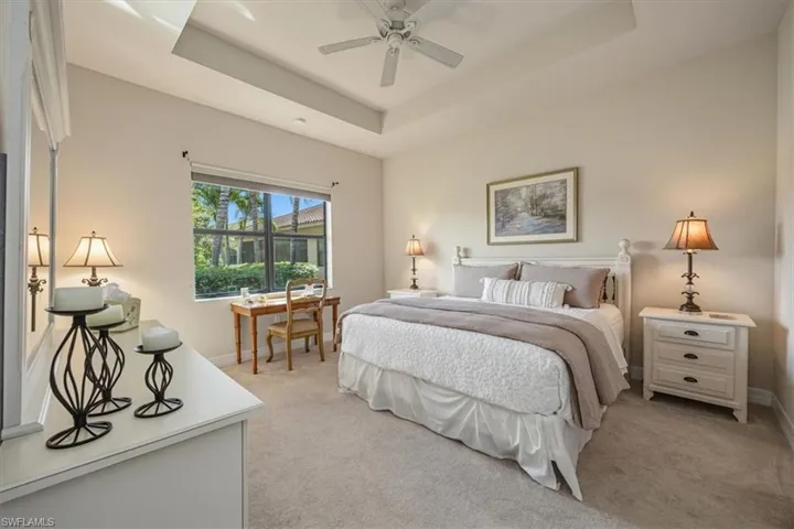 Bedroom with light colored carpet, a raised ceiling, and a ceiling fan