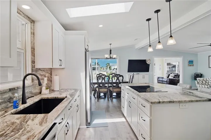 Kitchen featuring white cabinetry, hanging light fixtures, light stone counters, light wood finished floors, and a skylight