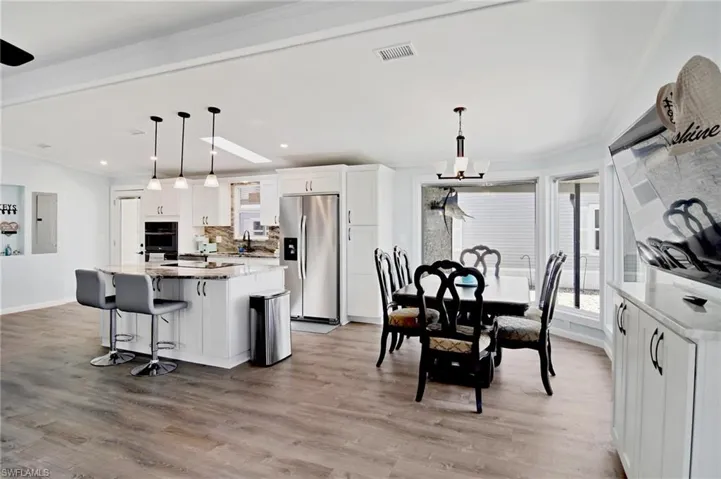 Kitchen with light stone countertops, white cabinetry, stainless steel fridge with ice dispenser, hanging light fixtures, and light wood finished floors