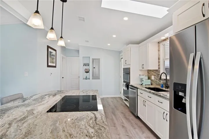 Kitchen with light stone counters, stainless steel appliances, white cabinets, pendant lighting, and recessed lighting