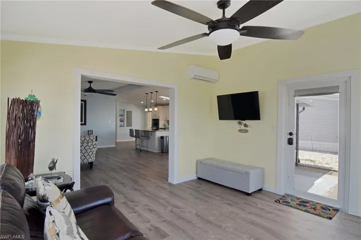 Living area with wood finished floors, a ceiling fan, crown molding, and a wall mounted AC