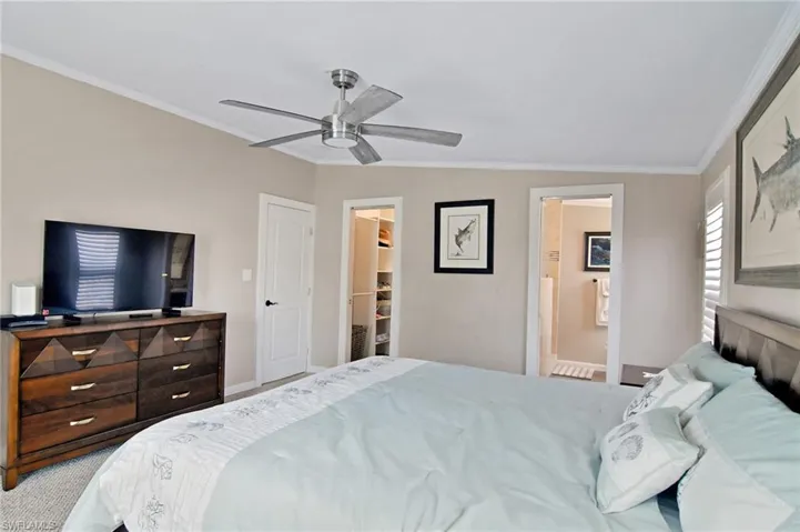 Carpeted bedroom with crown molding, a spacious closet, a ceiling fan, and ensuite bathroom
