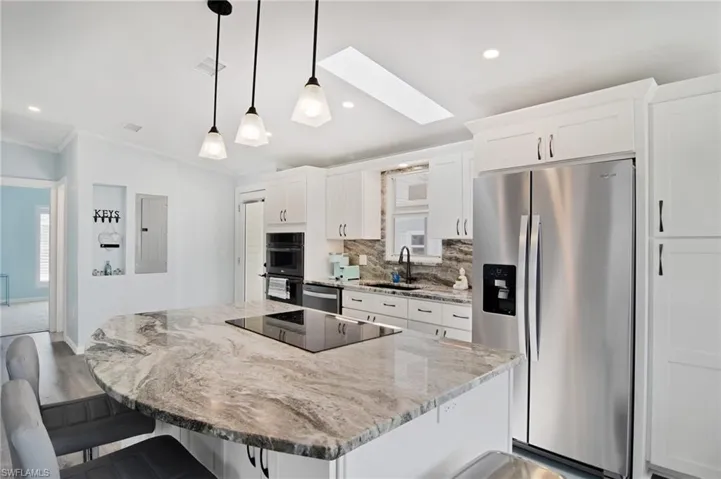 Kitchen with a skylight, black appliances, tasteful backsplash, light stone countertops, and a kitchen island