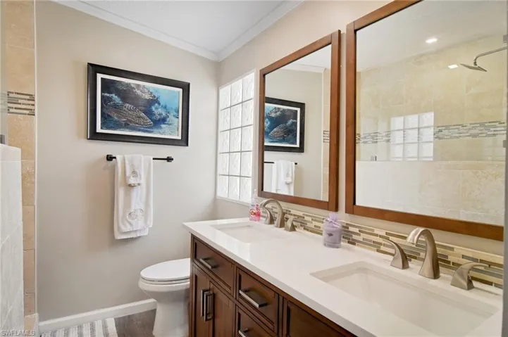 Full bath featuring double vanity, tasteful backsplash, a tile shower, and crown molding