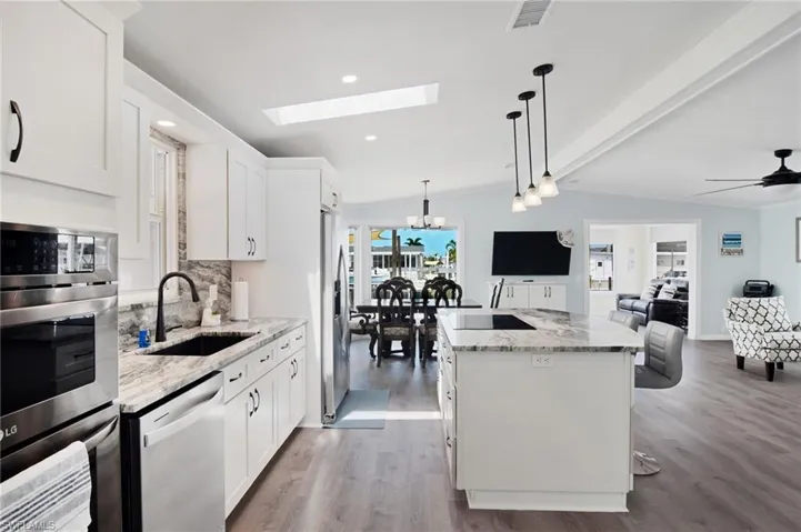 Kitchen with a kitchen island, appliances with stainless steel finishes, light stone countertops, a skylight, and tasteful backsplash