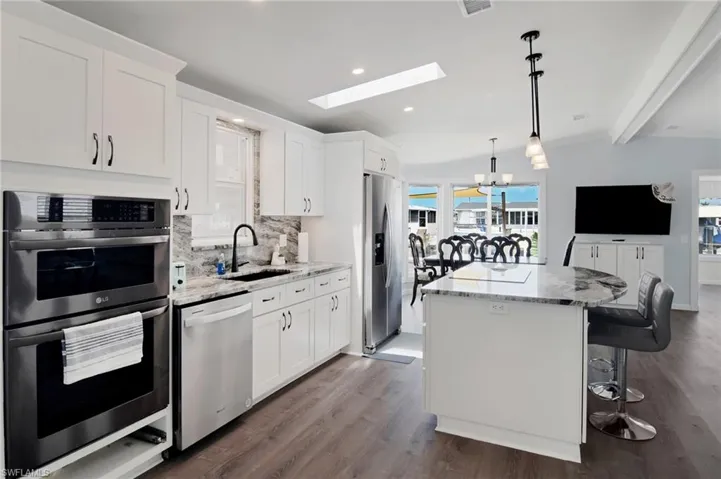 Kitchen featuring appliances with stainless steel finishes, light stone countertops, a skylight, a kitchen bar, and a kitchen island