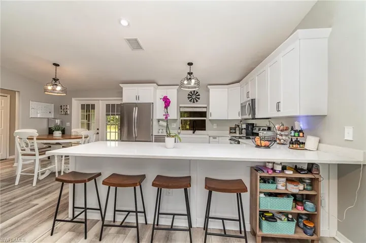Kitchen with decorative light fixtures, light hardwood / wood-style floors, kitchen peninsula, stainless steel appliances, and white cabinetry