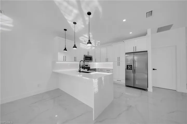 Kitchen with stainless steel appliances, white cabinetry, a peninsula, pendant lighting, and light stone countertops