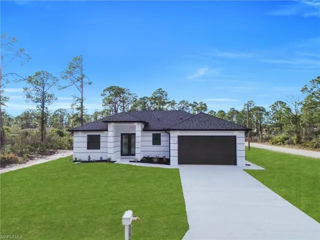 View of front of property with a front yard, concrete driveway, and a garage
