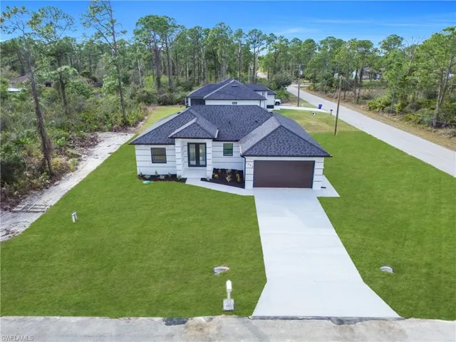 View of front of home featuring a front lawn, concrete driveway, roof with shingles, an attached garage, and view of wooded area