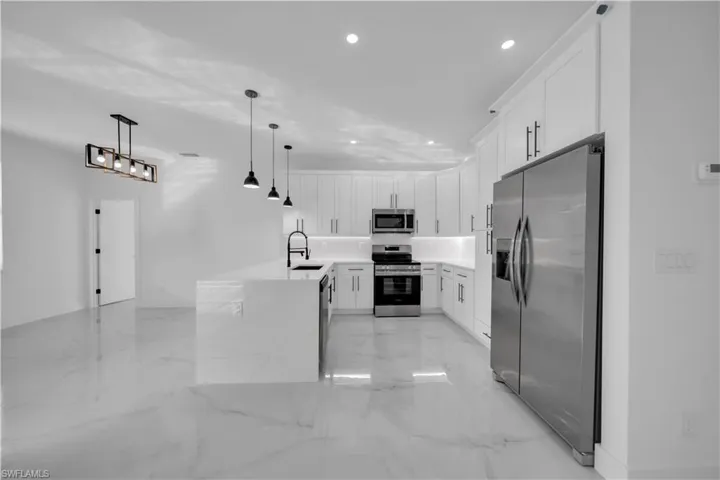 Kitchen featuring stainless steel appliances, white cabinetry, light stone counters, pendant lighting, and recessed lighting