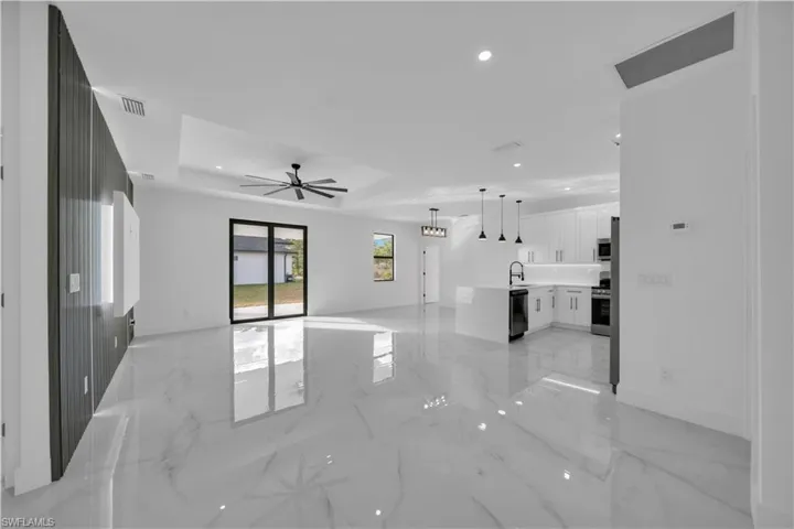 Unfurnished living room featuring recessed lighting, light marble finish floors, ceiling fan, a tray ceiling, and a chandelier