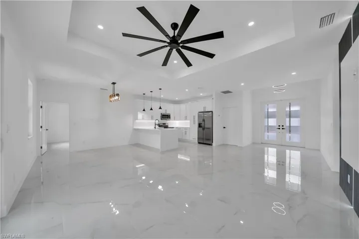 Unfurnished living room with french doors, a tray ceiling, recessed lighting, light marble finish flooring, and a ceiling fan