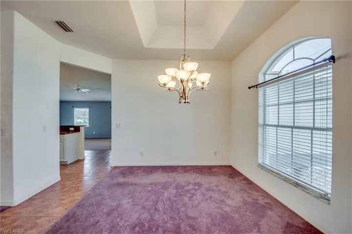 Unfurnished room with light tile patterned floors, a tray ceiling, and ceiling fan with notable chandelier