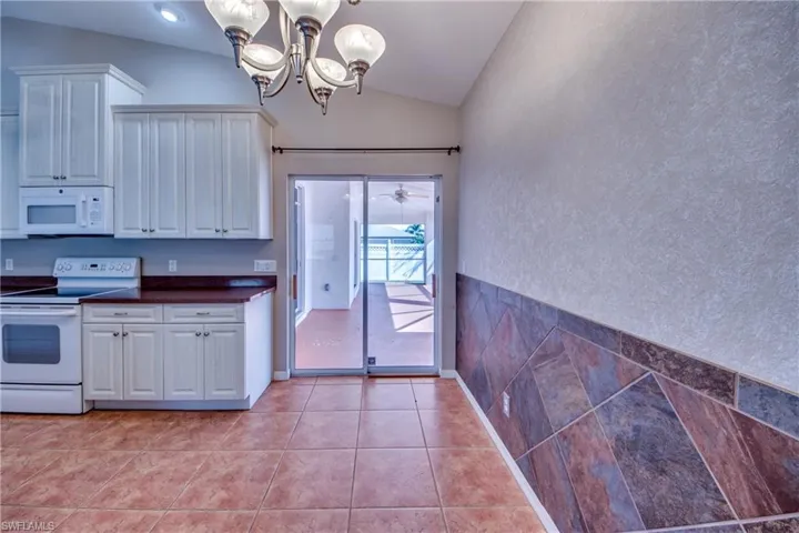 Kitchen featuring white appliances, white cabinets, light tile patterned flooring, ceiling fan with notable chandelier, and vaulted ceiling