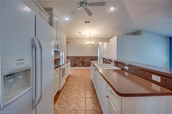 Kitchen featuring sink, decorative light fixtures, tile walls, light tile patterned floors, and white appliances