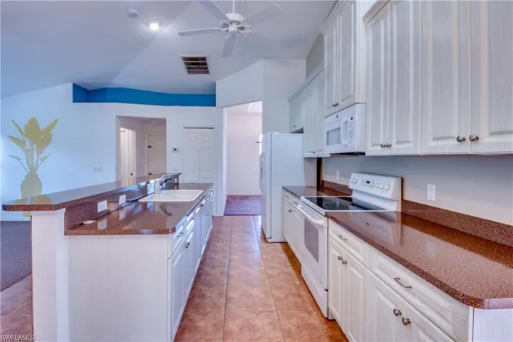 Kitchen featuring white cabinetry, white appliances, lofted ceiling, and sink