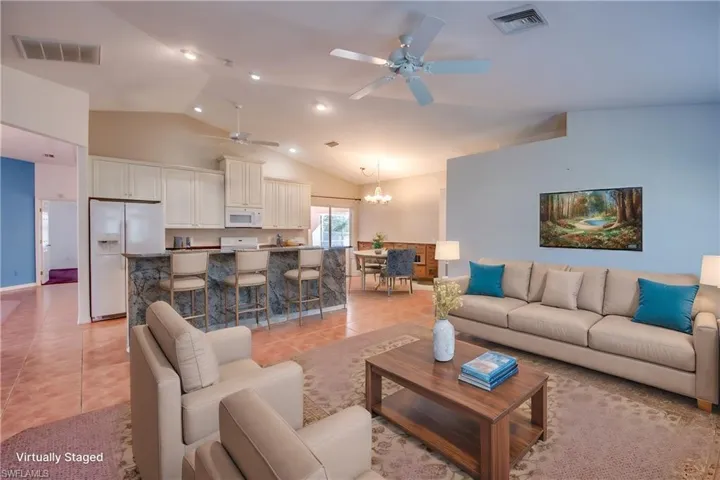 Living room with ceiling fan with notable chandelier, light tile patterned floors, and high vaulted ceiling