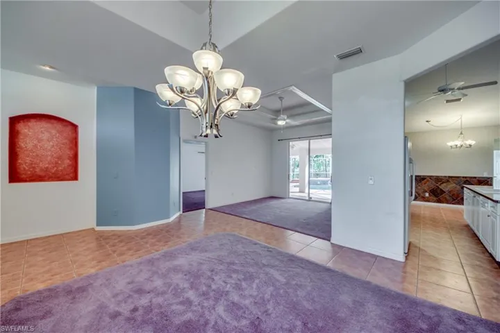 Tiled spare room featuring a tray ceiling and ceiling fan with notable chandelier