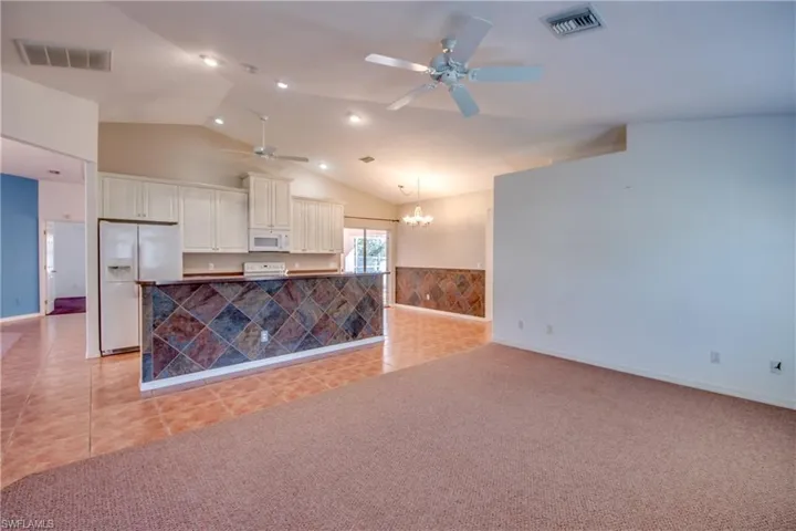 Kitchen with vaulted ceiling, decorative light fixtures, white cabinetry, light tile patterned floors, and white appliances