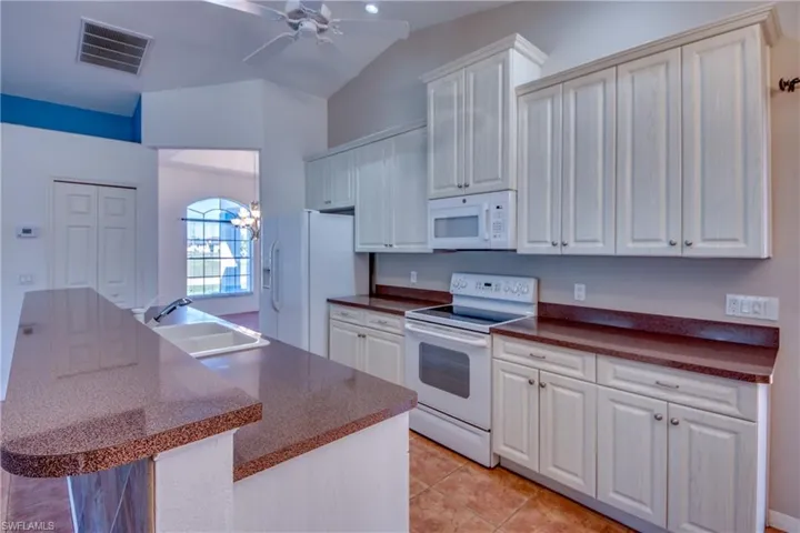Kitchen with sink, white appliances, light tile patterned floors, and white cabinets