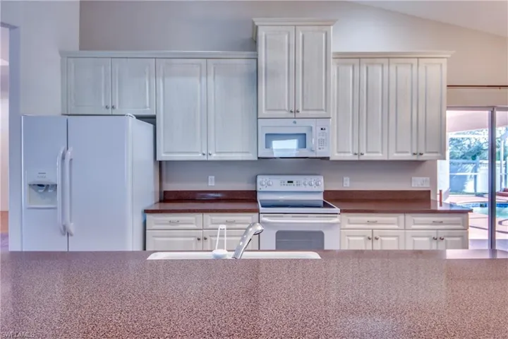 Kitchen featuring white cabinetry, lofted ceiling, sink, and white appliances