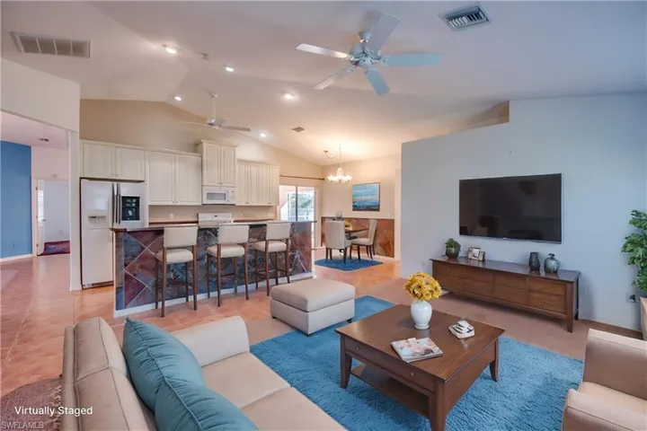 Tiled living room featuring lofted ceiling and ceiling fan with notable chandelier