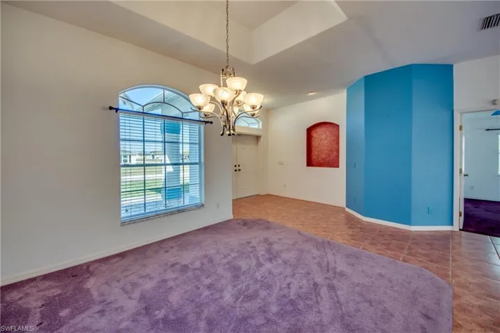 Tiled empty room featuring lofted ceiling and a chandelier