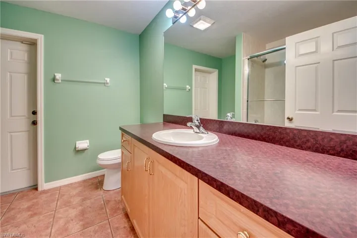 Bathroom with a shower with door, vanity, tile patterned floors, and toilet