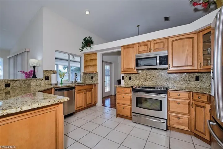 Kitchen featuring appliances with stainless steel finishes, light stone counters, lofted ceiling, decorative backsplash, and light tile patterned floors