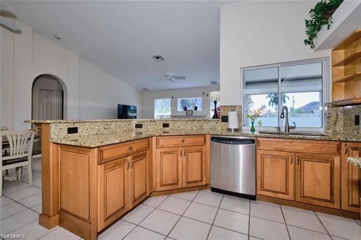 Kitchen featuring brown cabinetry, tasteful backsplash, stainless steel dishwasher, and light stone countertops