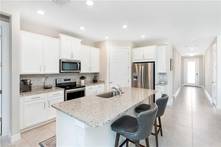 Kitchen with stainless steel appliances, white cabinetry, tasteful backsplash, light stone counters, and light tile patterned floors